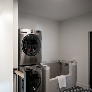 Ispirazione per una grande lavanderia multiuso scandinava con ante in stile shaker, ante nere, pareti grigie, pavimento con piastrelle in ceramica, lavatrice e asciugatrice a colonna e pavimento grigio