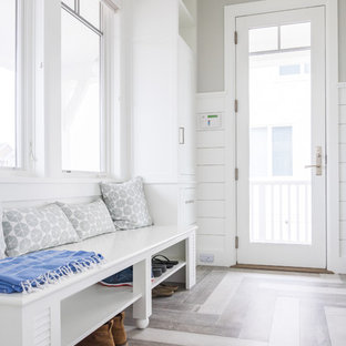 Foto på ett mellanstort maritimt vit l-format grovkök, med luckor med lamellpanel, vita skåp, träbänkskiva, vita väggar, ljust trägolv, en tvättmaskin och torktumlare bredvid varandra och grått golv