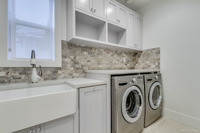 Inspiration for a transitional limestone floor laundry room remodel in Vancouver with a farmhouse sink, shaker cabinets, gray cabinets, quartz countertops and a side-by-side washer/dryer