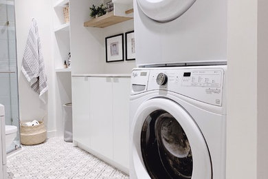 Example of a trendy porcelain tile laundry room design in Toronto with flat-panel cabinets, white cabinets, quartz countertops, white walls, a stacked washer/dryer and white countertops