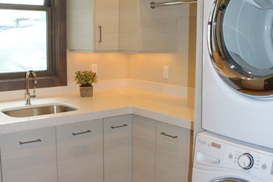 Inspiration for a mid-sized modern l-shaped medium tone wood floor dedicated laundry room remodel in Salt Lake City with an undermount sink, flat-panel cabinets, laminate countertops, beige walls, a stacked washer/dryer and light wood cabinets