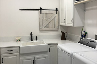 Inspiration for a mid-sized country l-shaped vinyl floor and gray floor dedicated laundry room remodel in Los Angeles with a farmhouse sink, raised-panel cabinets, white cabinets, quartz countertops, white walls, a side-by-side washer/dryer and white countertops