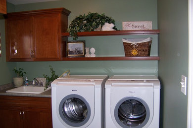 Foto de cuarto de lavado lineal tradicional pequeño con fregadero encastrado, armarios con paneles con relieve, puertas de armario de madera oscura, encimera de laminado, paredes verdes y lavadora y secadora juntas