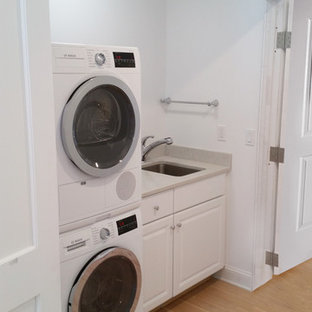 Laundry closet - mid-sized farmhouse single-wall light wood floor and beige floor laundry closet idea in New York with an undermount sink, raised-panel cabinets, white cabinets, laminate countertops, white walls and a stacked washer/dryer