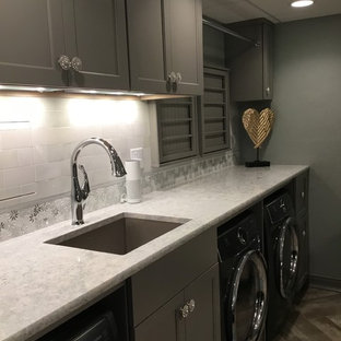 Idée de décoration pour une grand buanderie style shabby chic multi-usage avec un évier encastré, un placard avec porte à panneau encastré, des portes de placard grises, un plan de travail en quartz modifié, un sol en vinyl, des machines côte à côte, un sol marron et un plan de travail blanc.