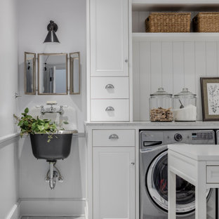 Inspiration för en maritim grå grått tvättstuga, med en allbänk, luckor med infälld panel, vita skåp, vita väggar, en tvättmaskin och torktumlare bredvid varandra och grått golv