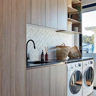 Immagine di una sala lavanderia minimal con lavello sottopiano, ante lisce, ante in legno scuro, pareti bianche, lavatrice e asciugatrice affiancate, pavimento grigio e top nero