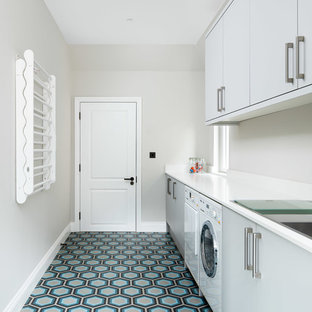 This is an example of a contemporary single-wall separated utility room in London with flat-panel cabinets, grey cabinets, grey walls, a side by side washer and dryer, multi-coloured floors and white worktops.