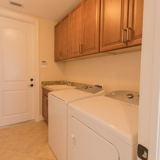 Réalisation d'une buanderie linéaire tradition dédiée et de taille moyenne avec un évier utilitaire, un placard avec porte à panneau surélevé, des portes de placard beiges, un plan de travail en granite, un mur beige, un sol en carrelage de porcelaine et des machines côte à côte.