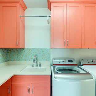 Exempel på en mellanstor modern l-formad tvättstuga enbart för tvätt, med luckor med infälld panel, orange skåp, bänkskiva i kalksten, vita väggar, en tvättmaskin och torktumlare bredvid varandra och en undermonterad diskho