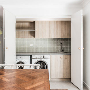 Inredning av en modern grå grått tvättstuga, med grönt stänkskydd, stänkskydd i cementkakel och en tvättmaskin och torktumlare bredvid varandra