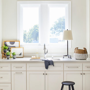 Immagine di una grande sala lavanderia chic con lavello sottopiano, ante in stile shaker, ante bianche, top in superficie solida, paraspruzzi bianco, paraspruzzi in lastra di pietra, pareti bianche, pavimento in gres porcellanato, lavatrice e asciugatrice affiancate, pavimento bianco e top bianco