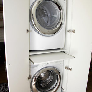 Example of a beach style laundry closet design in Miami with flat-panel cabinets, white cabinets and a stacked washer/dryer