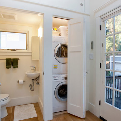 Laundry closet - small craftsman single-wall medium tone wood floor and brown floor laundry closet idea in San Francisco with a single-bowl sink, shaker cabinets, a stacked washer/dryer, white cabinets and white walls