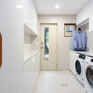 Idée de décoration pour une buanderie parallèle minimaliste dédiée et de taille moyenne avec un évier posé, un placard à porte plane, des portes de placard blanches, un plan de travail en quartz modifié, une crédence beige, une crédence en carreau de céramique, un mur beige, un sol en carrelage de céramique, des machines côte à côte, un sol beige et un plan de travail blanc.