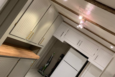 サンフランシスコにある低価格の中くらいなトラディショナルスタイルのおしゃれな家事室 (ll型、ドロップインシンク、シェーカースタイル扉のキャビネット、白いキャビネット、木材カウンター、グレーのキッチンパネル、セラミックタイルのキッチンパネル、グレーの壁、クッションフロア、左右配置の洗濯機・乾燥機、白い床、茶色いキッチンカウンター、表し梁、パネル壁) の写真