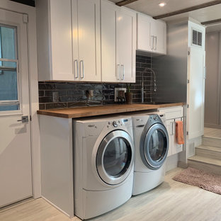Immagine di una lavanderia multiuso american style di medie dimensioni con lavello da incasso, ante in stile shaker, ante bianche, top in legno, paraspruzzi grigio, paraspruzzi con piastrelle in ceramica, pareti grigie, pavimento in vinile, lavatrice e asciugatrice affiancate, pavimento bianco, top marrone, travi a vista e pannellatura