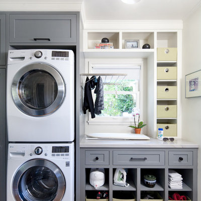 Large transitional single-wall medium tone wood floor laundry room photo in Santa Barbara with shaker cabinets, gray cabinets, white walls, a stacked washer/dryer and gray countertops