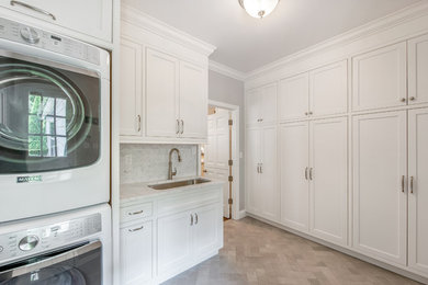 Inspiration for a mid-sized transitional l-shaped porcelain tile utility room remodel in New York with an undermount sink, beaded inset cabinets, white cabinets, marble countertops, gray walls and a stacked washer/dryer