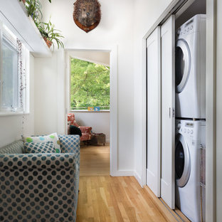 Example of a small trendy single-wall light wood floor laundry closet design in Raleigh with white walls and a stacked washer/dryer