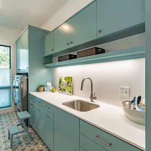 Inspiration för stora moderna linjära vitt tvättstugor enbart för tvätt, med en enkel diskho, släta luckor, bänkskiva i kvarts, beige väggar, klinkergolv i porslin, en tvättmaskin och torktumlare bredvid varandra, flerfärgat golv och turkosa skåp