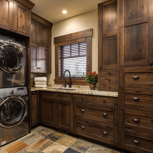 Immagine di una grande sala lavanderia stile rurale con lavello sottopiano, ante in stile shaker, ante in legno bruno, top in granito, pavimento in ardesia, lavatrice e asciugatrice a colonna, pareti beige e top beige