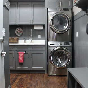 Inspiration for a mid-sized timeless single-wall dark wood floor dedicated laundry room remodel in Raleigh with a drop-in sink, shaker cabinets, gray cabinets, white walls and a stacked washer/dryer