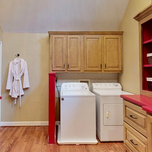 Inspiration pour une buanderie en U dédiée et de taille moyenne avec un placard avec porte à panneau surélevé, des portes de placard en bois clair, un plan de travail en surface solide, un mur beige, un sol en bois clair, des machines côte à côte et un plan de travail rouge.