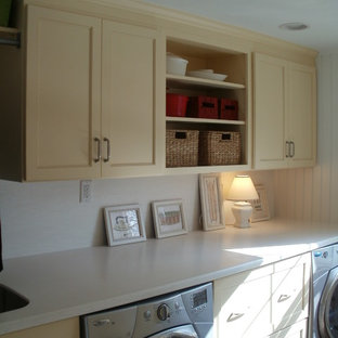 Inspiration pour une buanderie linéaire traditionnelle dédiée et de taille moyenne avec un plan de travail en surface solide, un sol en carrelage de porcelaine, un évier encastré, un placard à porte shaker, un mur blanc, des machines côte à côte, un sol marron et des portes de placard jaunes.