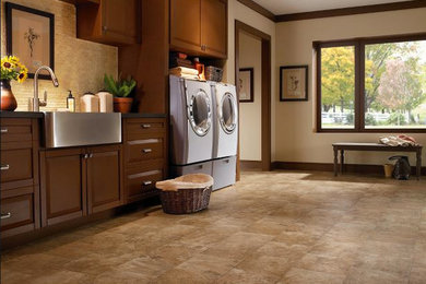 Example of a large trendy l-shaped vinyl floor dedicated laundry room design in San Francisco with a farmhouse sink, raised-panel cabinets, dark wood cabinets, solid surface countertops, beige walls and a side-by-side washer/dryer