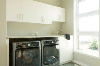 Modelo de cuarto de lavado moderno con paredes beige, suelo vinílico, lavadora y secadora juntas y suelo marrón