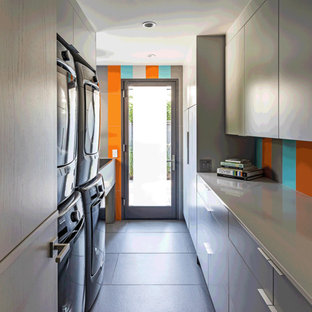 Immagine di una piccola sala lavanderia design con lavatoio, ante lisce, ante grigie, top in quarzo composito, pareti arancioni, pavimento con piastrelle in ceramica, lavatrice e asciugatrice a colonna, pavimento grigio e top grigio