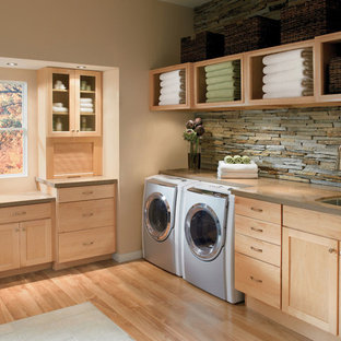 Immagine di una grande sala lavanderia tropicale con lavello sottopiano, ante in stile shaker, ante in legno chiaro, top in superficie solida, pareti beige, pavimento in legno massello medio e lavatrice e asciugatrice affiancate