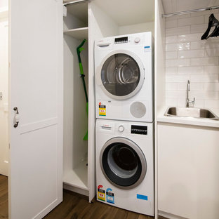 Exemple d'une petit buanderie linéaire chic avec un placard, un évier posé, des portes de placard blanches, un plan de travail en quartz modifié, un mur gris, sol en stratifié, des machines superposées, un plan de travail blanc et un placard à porte shaker.