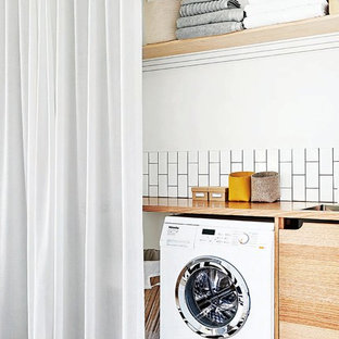 Idéer för att renovera ett litet minimalistiskt beige linjärt beige grovkök, med en nedsänkt diskho, släta luckor, skåp i mellenmörkt trä, träbänkskiva, vita väggar, målat trägolv, en tvättmaskin och torktumlare bredvid varandra och vitt golv
