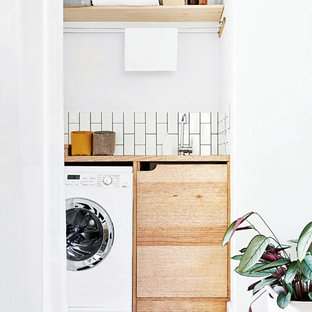 Réalisation d'une petit buanderie linéaire nordique multi-usage avec un évier posé, un placard à porte plane, des portes de placard en bois brun, un plan de travail en bois, un mur blanc, un sol en bois peint, des machines côte à côte, un sol blanc et un plan de travail beige.
