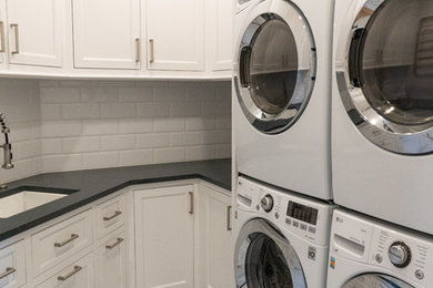 Mid-sized elegant u-shaped vinyl floor and multicolored floor dedicated laundry room photo in DC Metro with an undermount sink, recessed-panel cabinets, white cabinets, soapstone countertops, a stacked washer/dryer and gray countertops