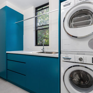 Esempio di una sala lavanderia minimalista di medie dimensioni con lavello sottopiano, ante turchesi, top in laminato, pareti grigie, lavatrice e asciugatrice a colonna, pavimento grigio e top bianco
