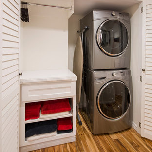 Inspiration for a mid-sized transitional single-wall medium tone wood floor and brown floor laundry closet remodel in Los Angeles with shaker cabinets, white cabinets, white walls and a stacked washer/dryer