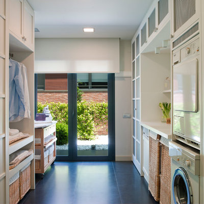 Example of a mid-sized transitional galley ceramic tile dedicated laundry room design in Barcelona with recessed-panel cabinets, white cabinets, solid surface countertops, white walls and a stacked washer/dryer