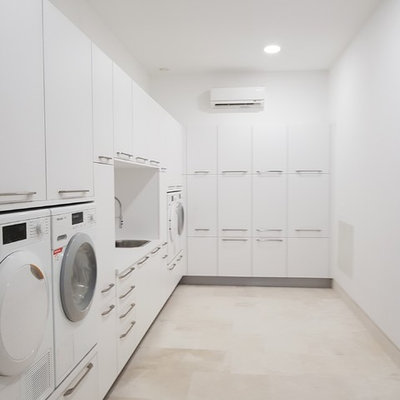 Large trendy l-shaped porcelain tile and beige floor laundry room photo in Malaga with flat-panel cabinets, white cabinets, laminate countertops, white backsplash, ceramic backsplash, white walls and a drop-in sink