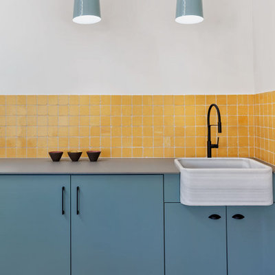 Example of a mid-sized danish single-wall porcelain tile and beige floor utility room design in Alicante-Costa Blanca with a drop-in sink, flat-panel cabinets, turquoise cabinets, quartz countertops, yellow walls, a concealed washer/dryer and gray countertops