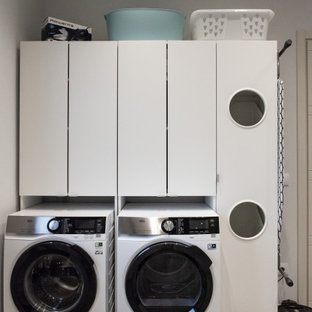 Exemple d'une buanderie linéaire moderne multi-usage et de taille moyenne avec un évier 2 bacs, un placard à porte plane, des portes de placard blanches, un plan de travail en bois, un mur beige, un sol en carrelage de porcelaine, des machines côte à côte, un sol gris et un plan de travail blanc.