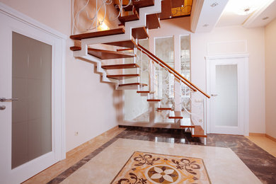 На фото: угловая лестница среднего размера в стиле неоклассика (современная классика) с деревянными ступенями и металлическими перилами с