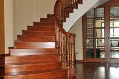 Идея дизайна: огромная изогнутая деревянная лестница в классическом стиле с деревянными ступенями и деревянными перилами