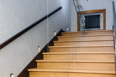 Imagen de escalera en U contemporánea pequeña con escalones de madera, contrahuellas de madera, barandilla de vidrio y papel pintado
