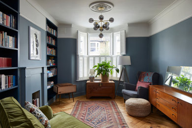 ロンドンにあるお手頃価格の小さなトランジショナルスタイルのおしゃれな独立型リビング (ライブラリー、青い壁、無垢フローリング、標準型暖炉、漆喰の暖炉まわり、茶色い床、白い天井) の写真