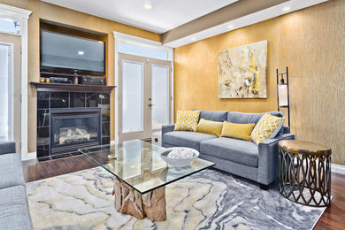 Mittelgroßes, Abgetrenntes Modernes Wohnzimmer mit gelber Wandfarbe, braunem Holzboden, Kamin, Kaminumrandung aus Stein und freistehendem TV in Calgary