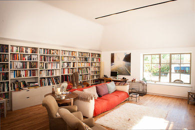 Aménagement d'un grand salon campagne ouvert avec une bibliothèque ou un coin lecture, un mur blanc, parquet clair et un téléviseur indépendant.