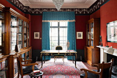 Imagen de despacho clásico grande con paredes rojas, suelo de madera oscura, todas las chimeneas, marco de chimenea de piedra y suelo marrón